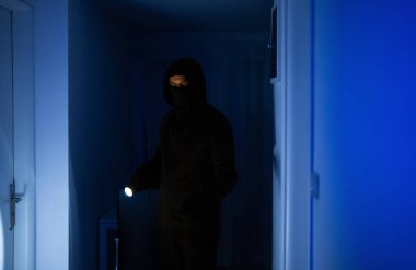 El feneri taşıyan maskeli soyguncu evini kontrol ediyor..
