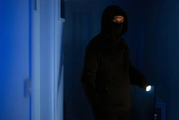 Masked robber with flashlight torch checking apartment.