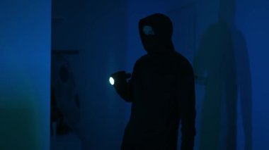 El feneri taşıyan maskeli soyguncu evini kontrol ediyor..