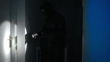 El feneri taşıyan maskeli soyguncu evini kontrol ediyor..