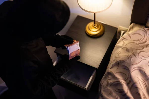 Female thief steals money from the bedside table.
