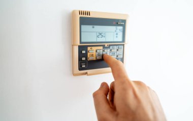 Adamın eli duvara monte edilmiş dijital termostatı ayarlıyor.