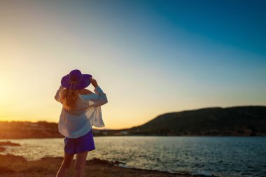 Gün batımında deniz kenarında mavi şapkalı bir kadın.