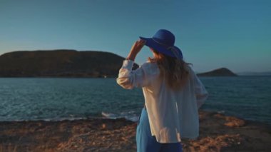Gün batımında deniz kenarında mavi şapkalı bir kadın.