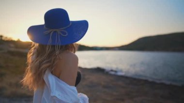 Gün batımında deniz kenarında mavi şapkalı bir kadın.
