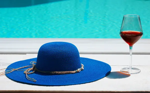 Havuzun önünde yaz şapkası ve bir bardak şarap. Tatil kavramı.