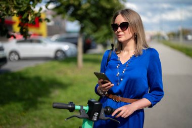 Sokakta elektrikli scooter 'ın yanında akıllı telefonu olan bir kadın..