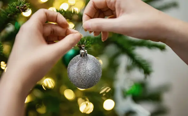 Woman hangs a ball on a New Year tree.