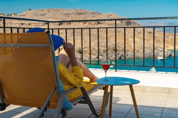 Bir bardak şarabı olan kadın, denize bakan bir balkonda dinleniyor..