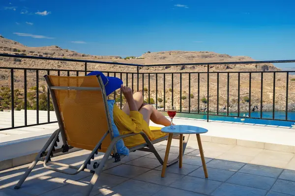 Bir bardak şarabı olan kadın, denize bakan bir balkonda dinleniyor..