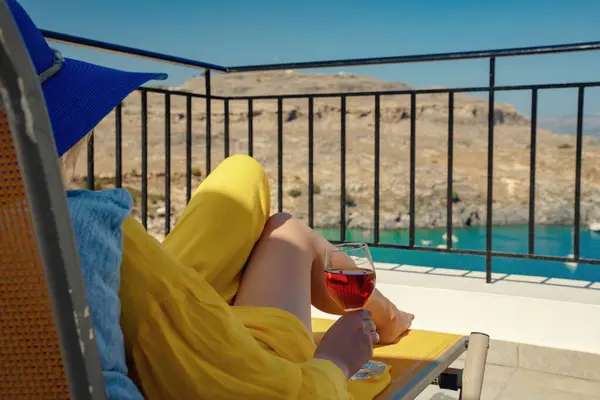 Bir bardak şarabı olan kadın, denize bakan bir balkonda dinleniyor..