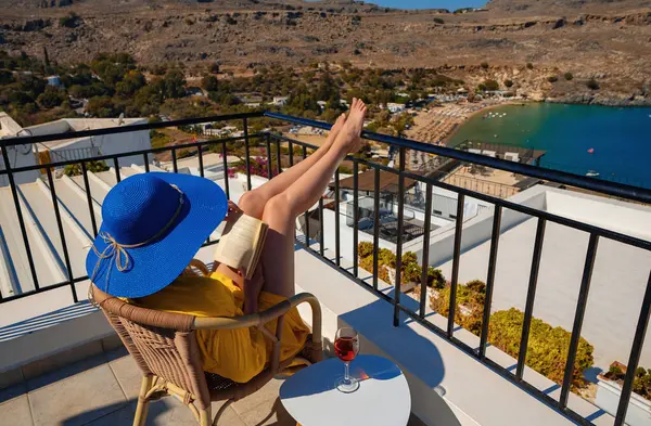 Kadın, denize bakan bir balkonda kitap okuyor..