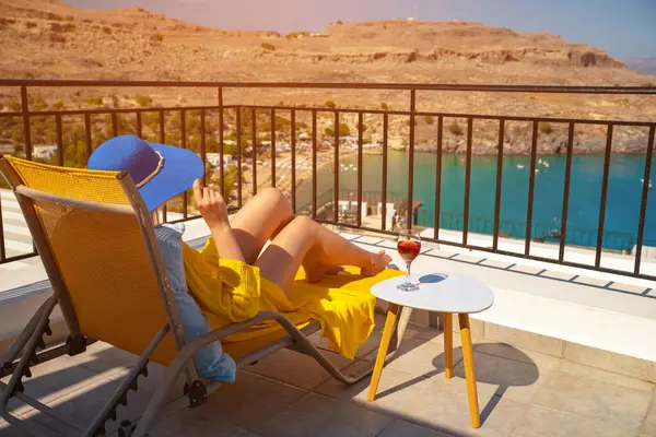 Bir bardak şarabı olan kadın, denize bakan bir balkonda dinleniyor..