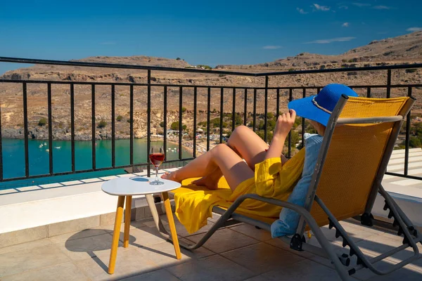 Bir bardak şarabı olan kadın, denize bakan bir balkonda dinleniyor..