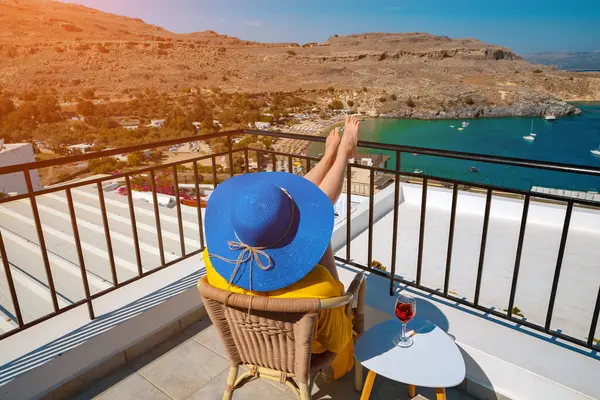 Bir bardak şarabı olan kadın, denize bakan bir balkonda dinleniyor..