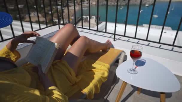 女性は海を見下ろすバルコニーの本を読みます — ストック動画