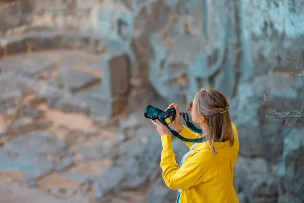 Female tourist takes photographs of Exedra at the entrance to the Acropolis of Lindos.