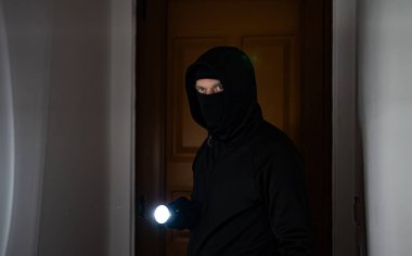 El feneri taşıyan maskeli soyguncu evini kontrol ediyor..
