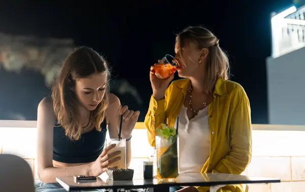 Two girls with cocktails at rooftop bar.