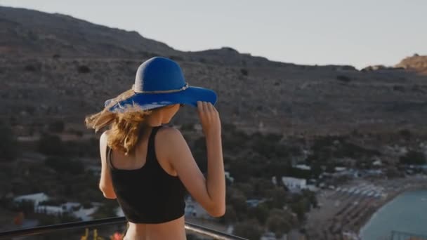 青い帽子の少女はバルコニーに立ってビーチを見る — ストック動画