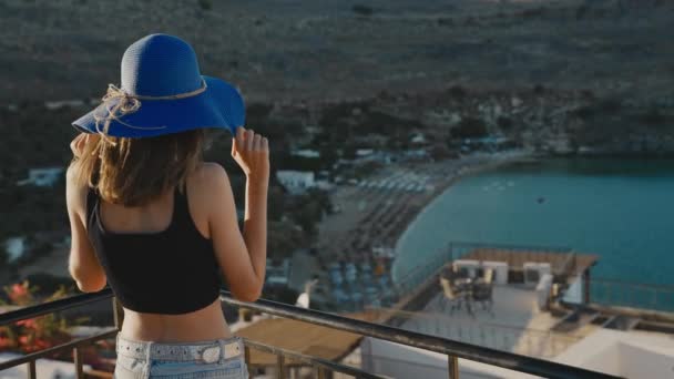 Κορίτσι Μπλε Καπέλο Στέκεται Στο Μπαλκόνι Και Κοιτάζει Την Παραλία — Αρχείο Βίντεο
