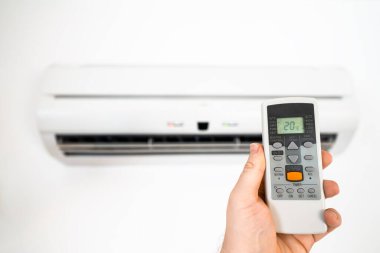 Klimanın önünde uzaktan kumandayı tutuyor..