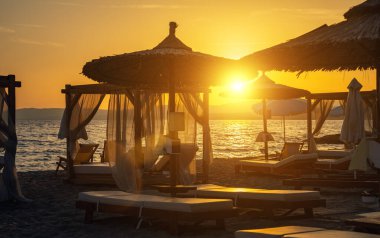 Plaj kabinleri ve güneş batarken deniz kenarında güneşlenirler..