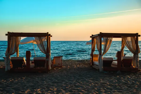 stock image Beach cabana beds and sun loungers on the seashore at sunset.