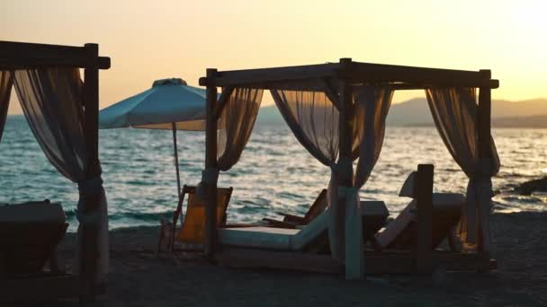 日没の海岸のビーチカバナベッドとサンラウンジャー — ストック動画