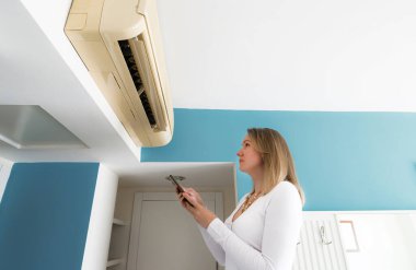 Telefonundaki uzaktan kumandayla akıllı bir klimayı kontrol eden bir kadın..