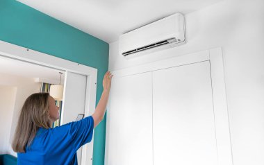 Telefonundaki uzaktan kumandayla akıllı bir klimayı kontrol eden bir kadın..