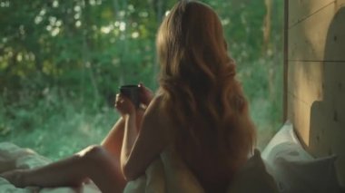 Ormandaki bir evin büyük panoramik penceresinin önündeki kadın..