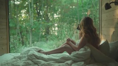 Ormandaki bir evin büyük panoramik penceresinin önündeki kadın..