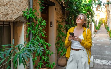 Akıllı telefonlu kadın turist eski şehirde yürüyor..