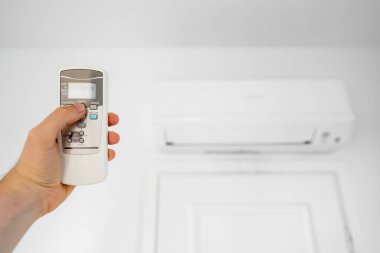 Adamın eli uzaktan kumandayı klimaya doğru yönlendiriyor..