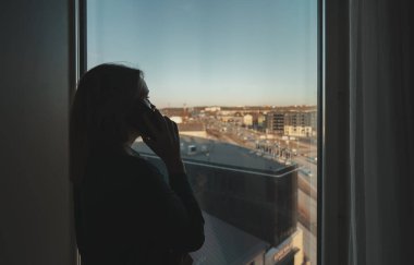 Ofis penceresinin önünde telefonla konuşan bir kadının silüeti..