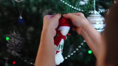 Yapay Noel ağacını kardan adam şeklinde bir oyuncakla süsleyen bir çocuğun elleri. Tatil için hazırlık atmosferi.