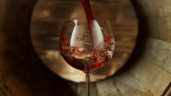 Pouring red wine into glass inside old wooden barrel. Concept of fresh beverages.