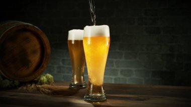 Glass of light beer pouring on wooden table. Still life shot with wooden keg on background.