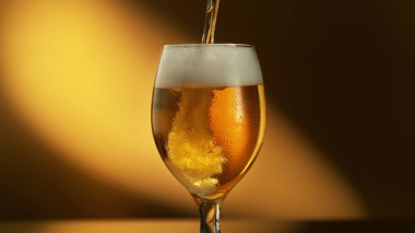 Glass of light beer pouring on shiny dark gold background. Studio shot with isolated glass of beer. clipart