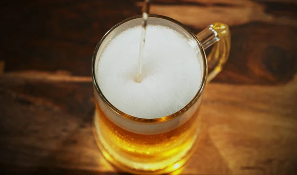 Glass of light beer pouring on wooden table. Studio shot with isolated glass of beer.