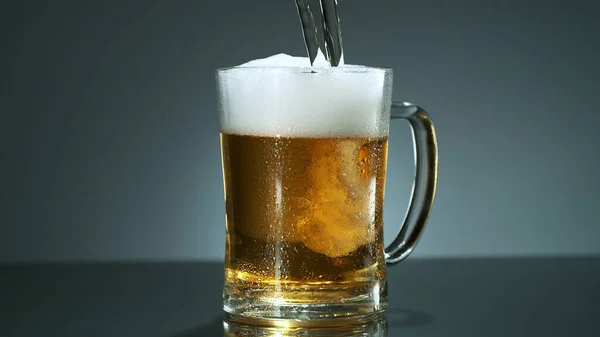 Glass of light beer pouring on shiny dark background. Studio shot with isolated glass of beer.