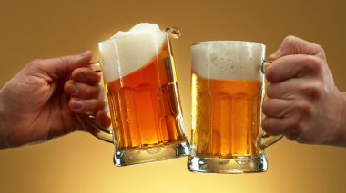 Two glasses of beer in cheers gesture, splashing out. Isolated on golden background.