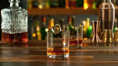 Super slow motion of falling ice cube into whisky with speed motion. Filmed on high speed cinema camera, 1000 fps, placed on high speed cine bot. Bar with bottles on background.