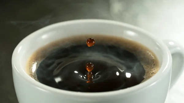 Detail of coffee drop falling into cup of coffee. Macro shot of black hot coffee drink.