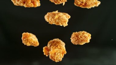 Siyah arka planda uçan kızarmış tavuk parçaları. Yüksek hızlı sinema kamerasında çekildi, 1000fps, yüksek hızlı sinüs robotuna yerleştirildi. Kamera hareket halinde, takip eden nesneler.