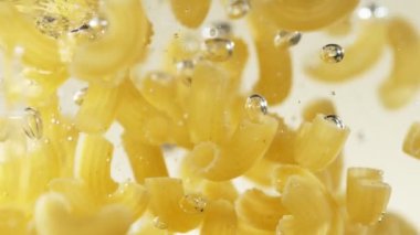 Super slow motion of flying Italian pasta pipe rigate into water. Filmed on high speed cinema camera, 1000 fps.