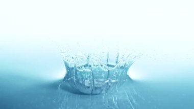 Mavi arka planda izole edilmiş, taç şeklinde su sıçratan süper yavaş çekim. Yüksek hızlı sinema kamerası, 1000 fps..