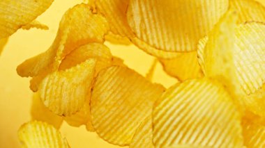 Patates cipsi havada uçuşuyor. Uçan abur cuburlar sarı arka planda izole.