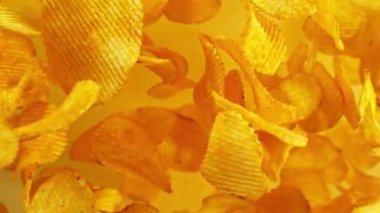 Sarı arka planda uçan kızarmış patates cipsleri süper yavaş çekimde. Yüksek hızlı sinema kamerası, 1000 fps. Kamera yüksek hızlı sinüs robotuna yerleştirilmiş, hedefi takip ediyor. Hız rampası etkisi.